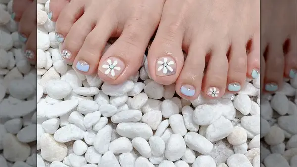 A close-up of a classic French pedicure with a floral accent by white_spa_nail