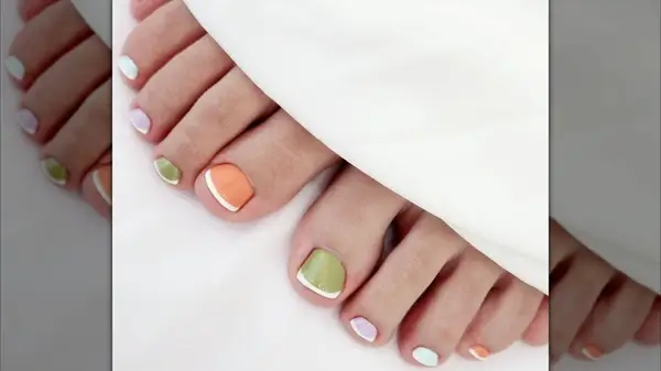A close-up of a French pedicure with a different vibrant base on each toe and classic white tips by 8.nail_