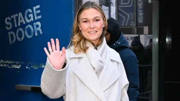 Julia Stiles waving in a cream wool coat
