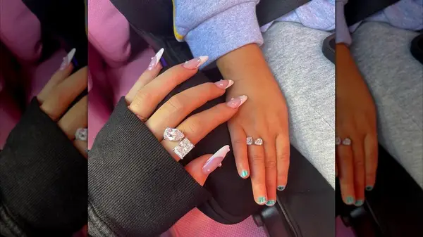 An adult hand with pearl-adorned French tips touching a child