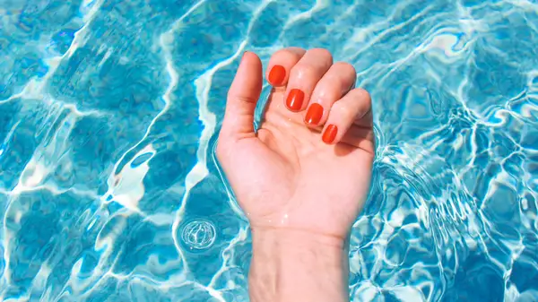 A hand with red fingernails and with water in the background