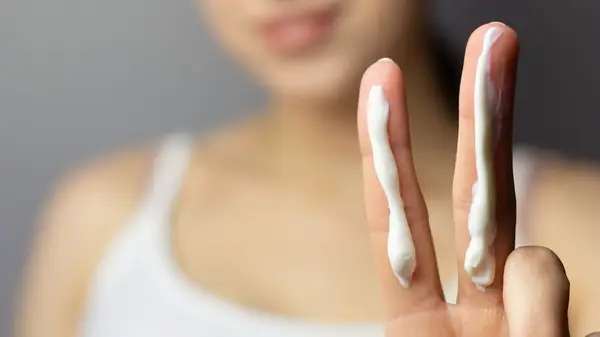 Woman holding up two fingers with sunscreen on them