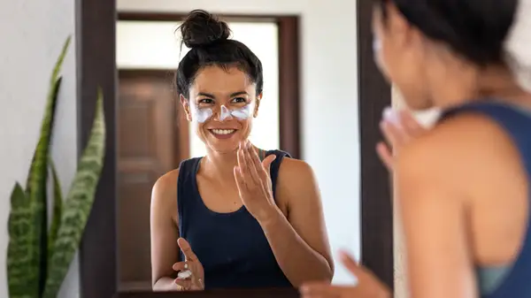 Woman smiling and applying sunscreen to face