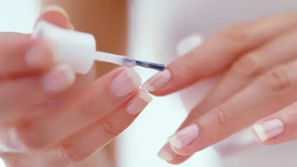 Hands applying clear polish to nails