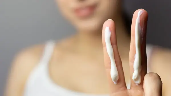 Woman holding up two fingers with sunscreen on them