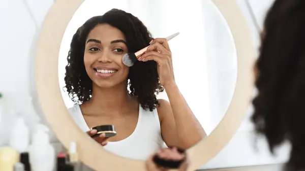 A girl using blush brush along cheekbones