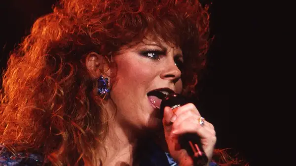 Reba McEntire singing into a microphone wearing heavy makeup