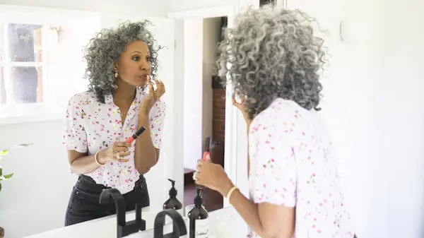 Woman with gray curly hair applies makeup
