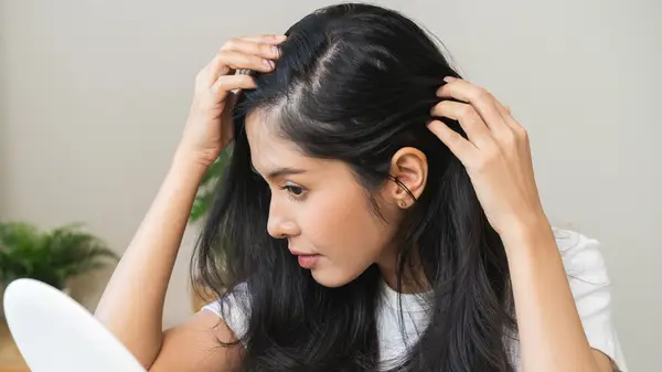 A woman examines her scalp and hair in a small mirror