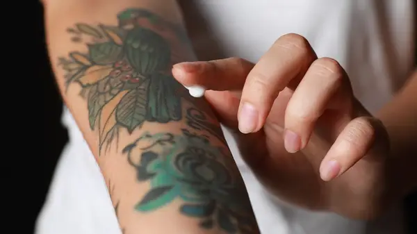 A woman puts a small dollop of cream on a new arm tattoo 