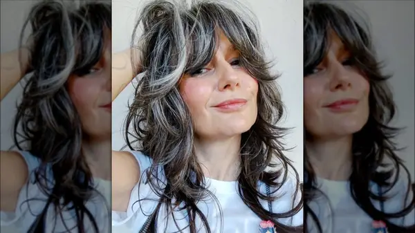 A woman with long layers and bangs with grey hair