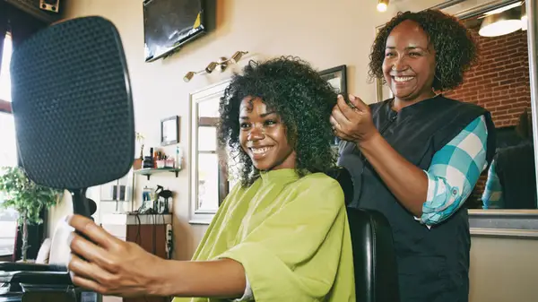 Woman with curly hair at salon holding up mirror