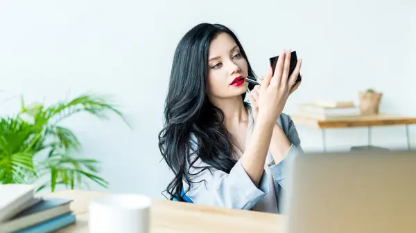 Woman applying red lipstick in her office