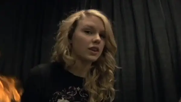 A still of curly-haired Taylor Swift working behind-the-scenes for the music video of 