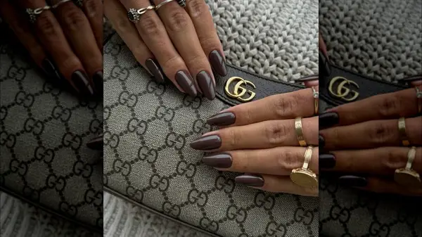 Two hands with mocha brown nails posed against a luxury handbag