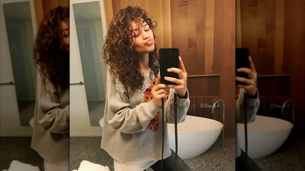Zendaya posing for a mirror selfie with curly hair