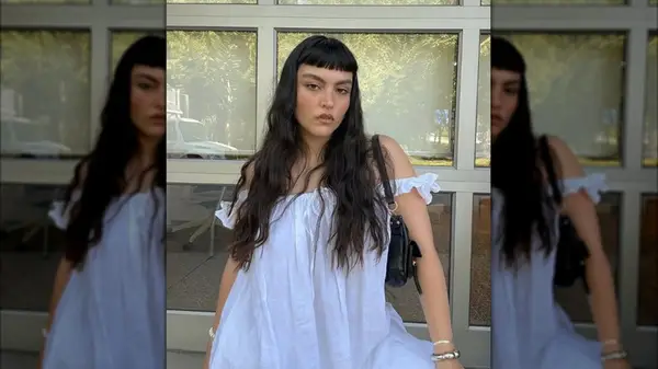 A woman wearing a white nightgown with long dark hair with blunt baby bangs
