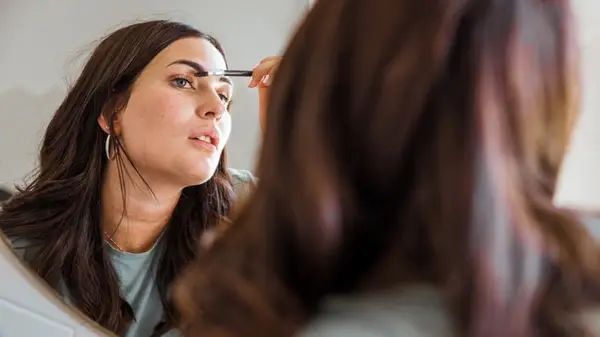 Woman doing her eyebrows in the mirror