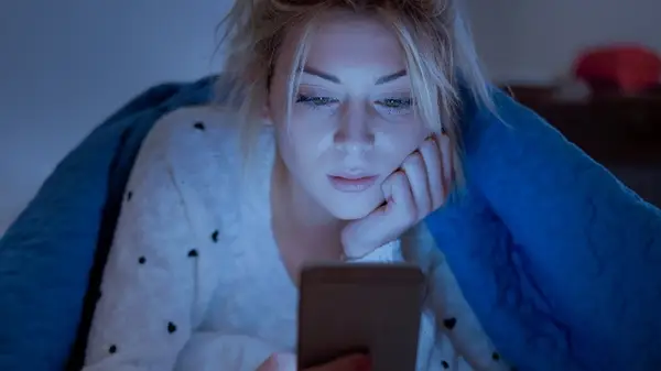 Woman on phone under a blanket