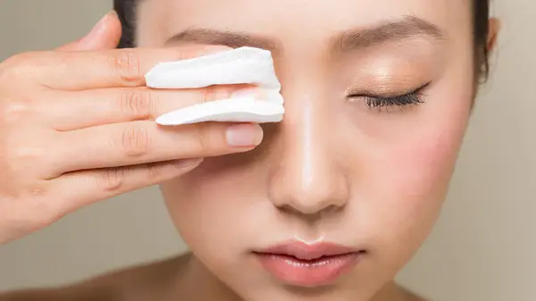 woman wiping off mascara with cotton pad
