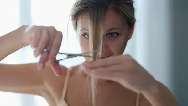 A woman cutting her own bangs in front of a pink background