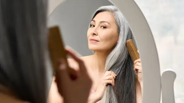 Woman combs hair in mirror