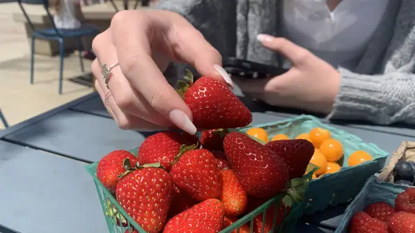 Close-up of hands with manicure picking up a strawberry