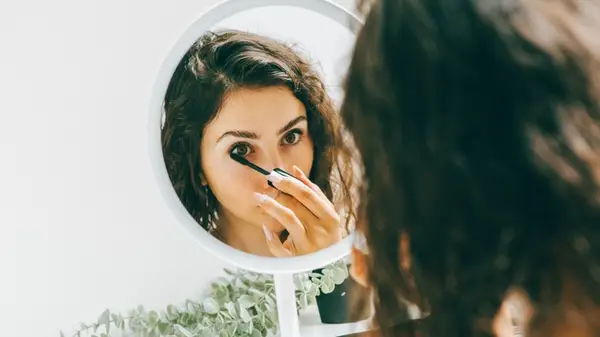 A woman applying mascara in a mirror
