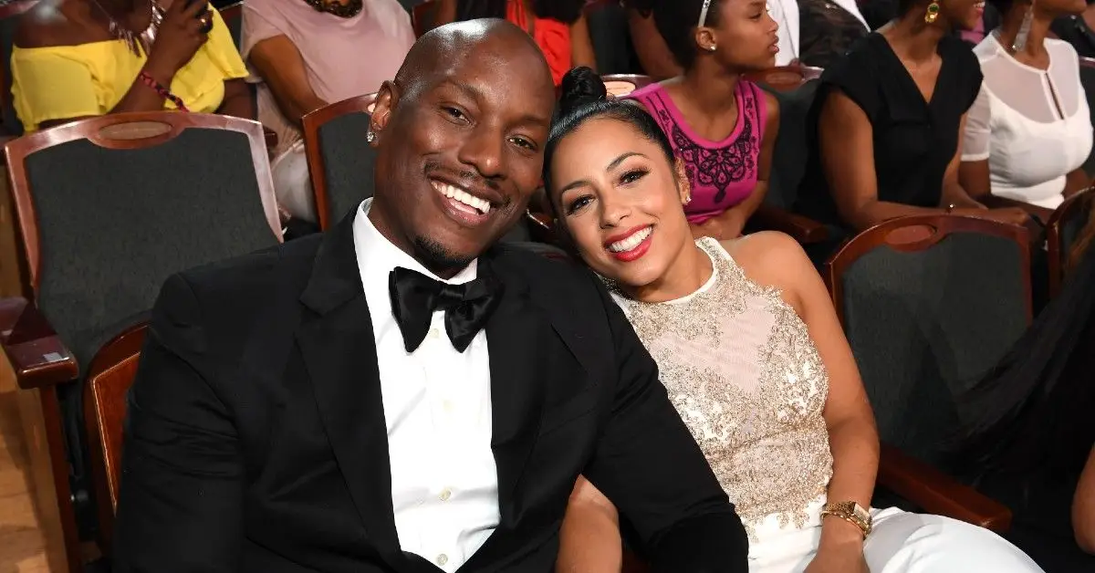 Tyrese Gibson con esmoquin blanco y negro sentada junto a Samantha Lee con un vestido de encaje blanco en la entrega de premios