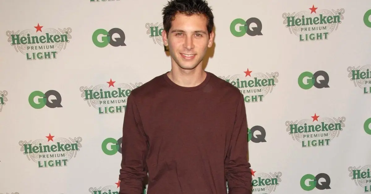 Justin Berfield lächelt in einem braunen Pullover