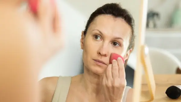 A woman applying foundation using a mirror