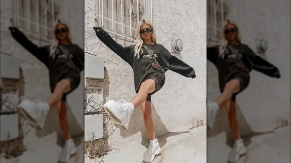 A girl wearing a sweatshirt, shorts and platform sneakers dancing in front of a wall