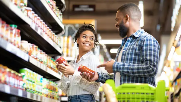 A couple at the grocery store together with the woman holding marinara sauce, looking back at the man smiling