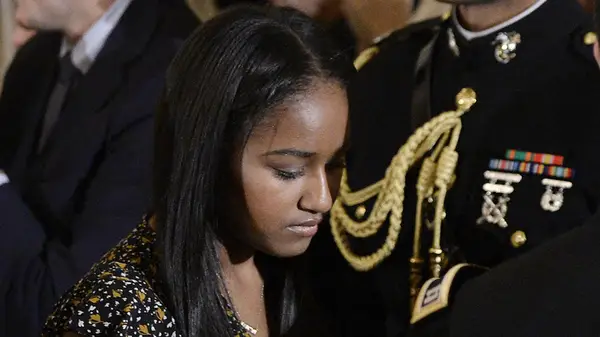 Sasha Obama standing in front of a man in uniform and looking down