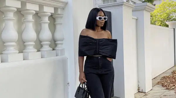 woman poses in front of gate wearing all black outfit