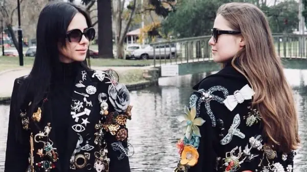 Two women wearing jackets with many brooches