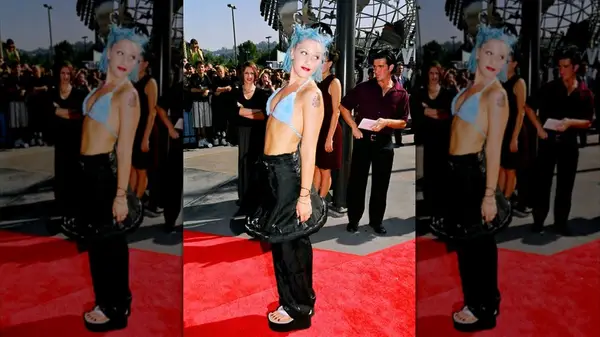 Gwen Stefani on the red carpet in a black skirt over pants and a blue bikini top with blue hair