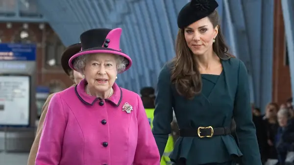 Queen Elizabeth II in pink and Catherine, Princess of Wales, in green and black, walking together outside