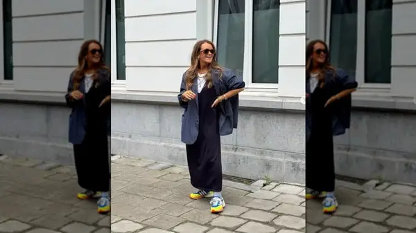 A woman standing on the steet wearing a navy blue dress and blazer with neon shoes