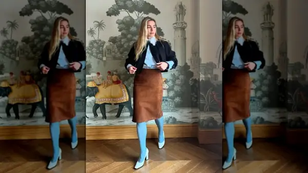 A woman in front of wall paper wearing a brown skirt, black top and blue shirt and tights