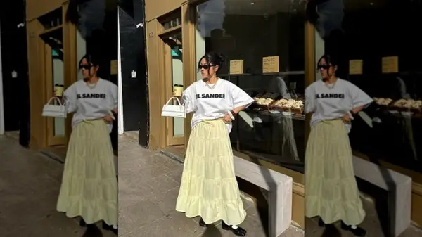 A woman on the street with an oversized white tee and a maxi length pastel yellow skirt