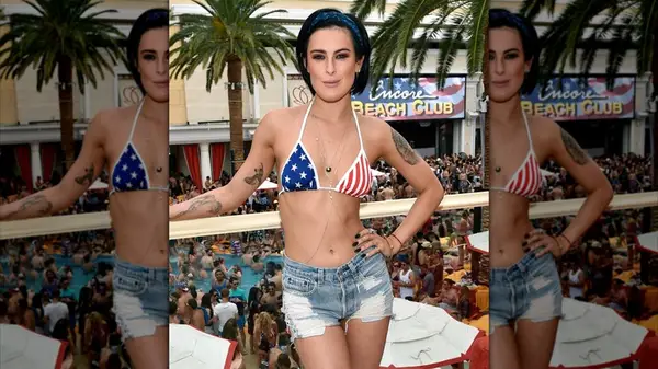 Rumer Willis leaning on a railing wearing an American flag bikini top and cutoff shorts