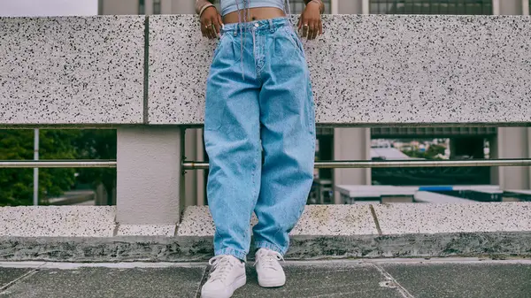 Woman standing in white chunky sneakers and loose fitting jeans