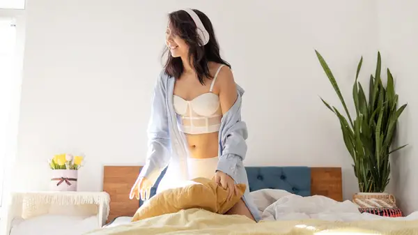 Woman wearing headphones in on bed in her underwear