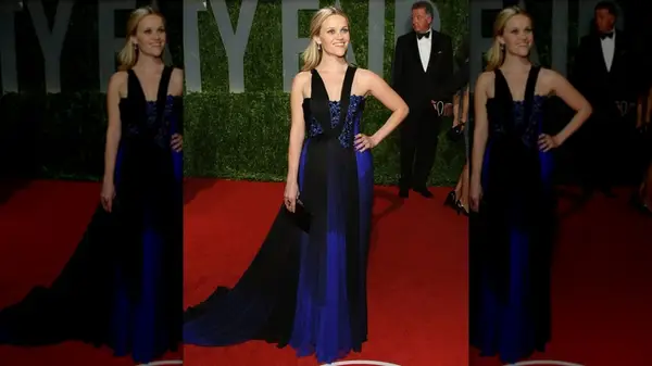 Reese Witherspoon posing with her hand on her hip, smiling while wearing a black and blue dress