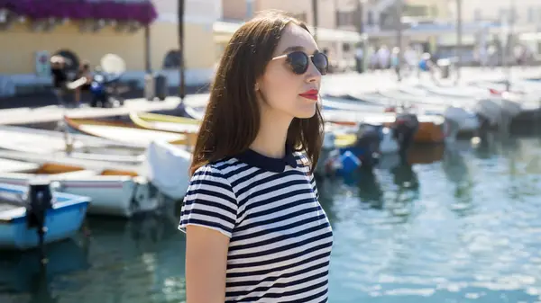 Woman wears striped shirt in front of boats