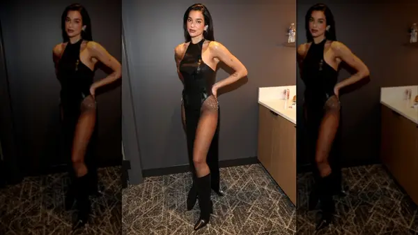 Dua Lipa posing in a black dress with fishnets and boots