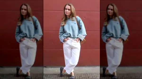 A woman wearing white jeans and a blue sweatshirt in front of a red wall
