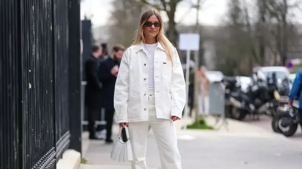 A woman standing on the street wearing white jeans and a white denim jacket