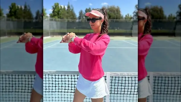 Eli Pironkova poses in a pink sweater on a tennis court